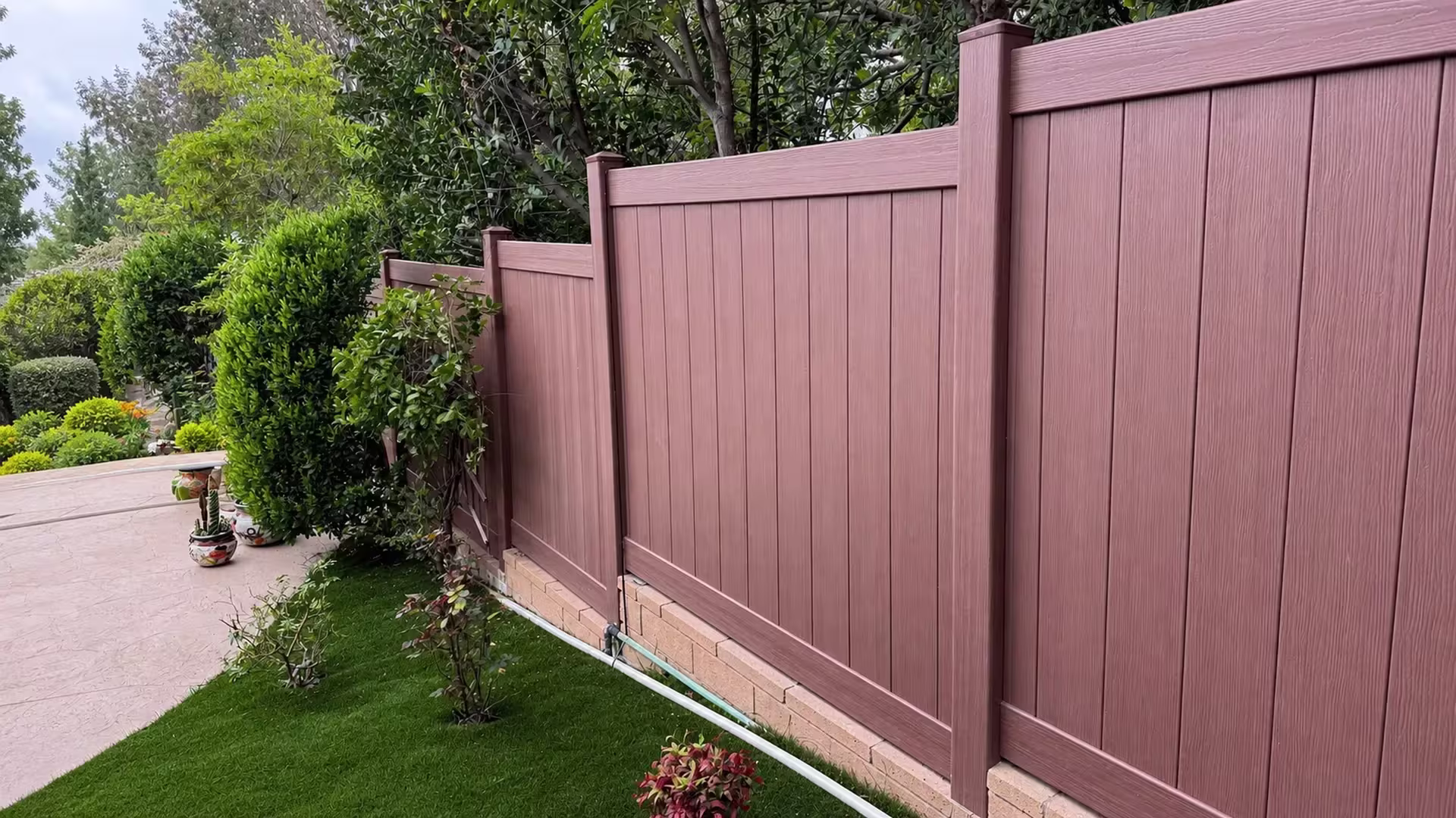 Five posts step down a sloped garden in this Brazilian Blend vinyl privacy fence beside a tan brick base wall