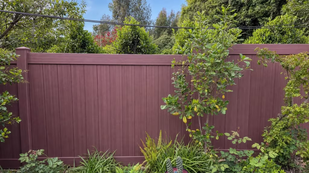 Two stepped runs of Brazilian Blend vinyl privacy fence meet behind a tree in this dense rose and fern garden
