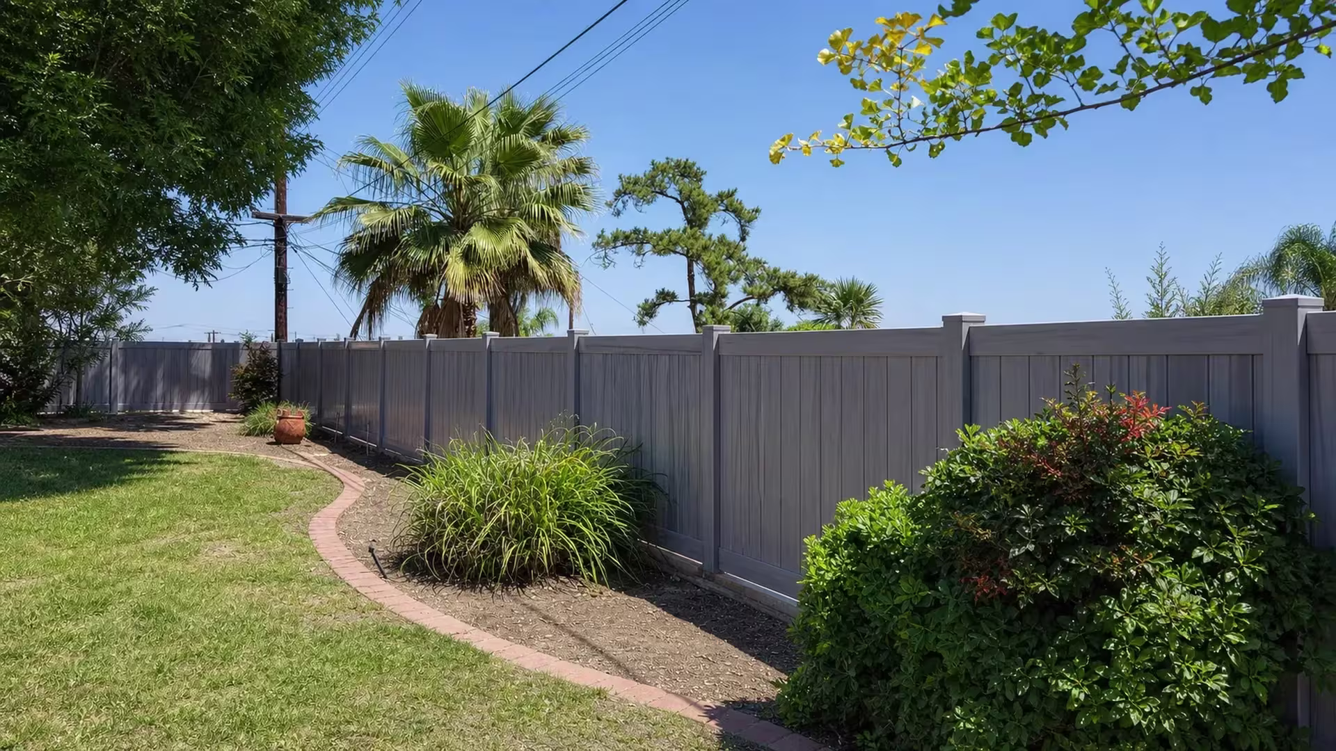 This Coastal Cedar vinyl privacy fence runs diagonally past a terracotta planter and a curved brick garden path