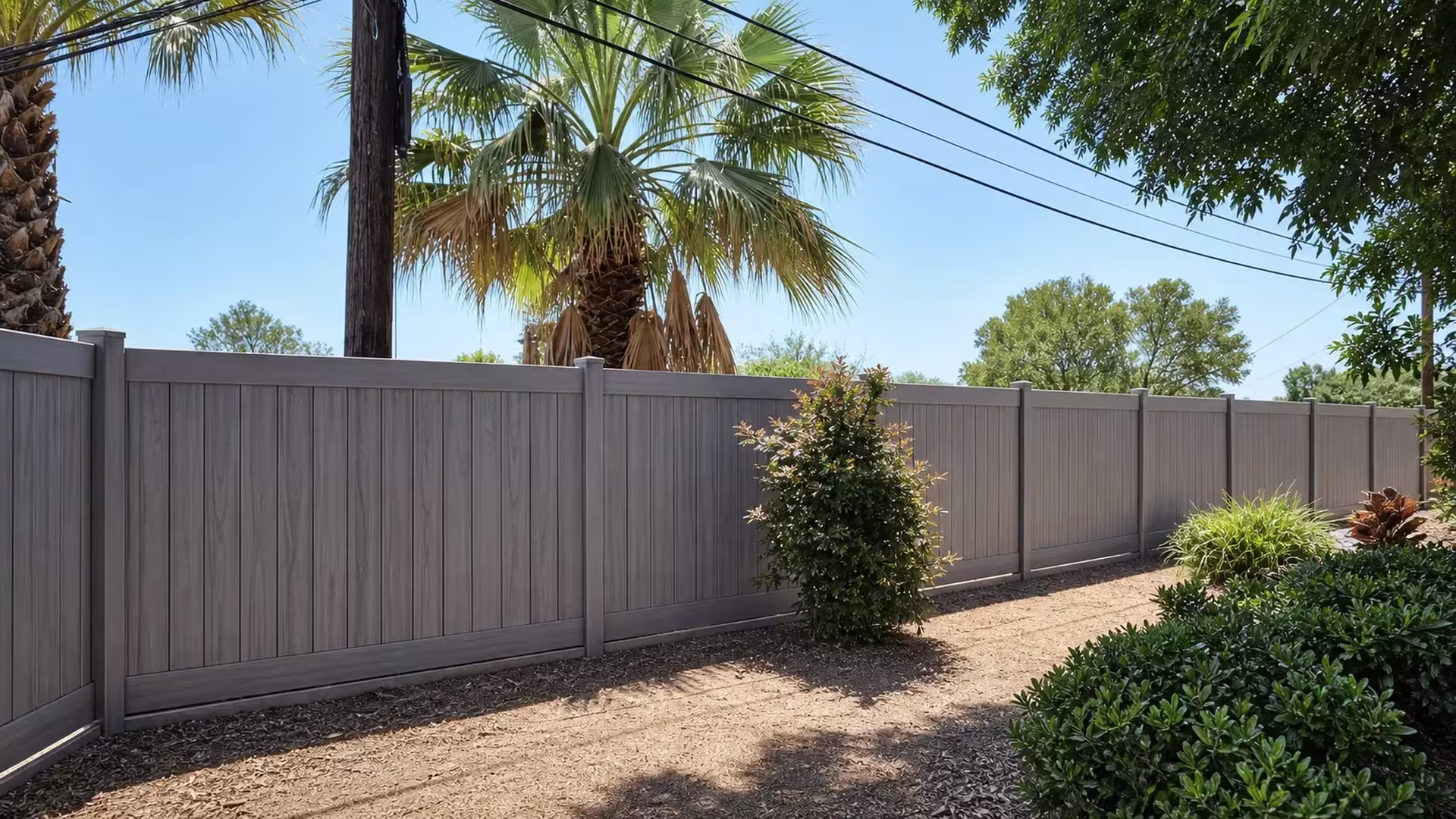 Five square posts with shallow caps mark this Coastal Cedar vinyl privacy fence receding across the yard