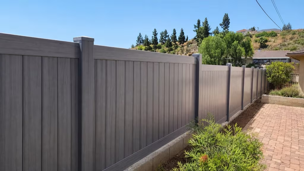 A low concrete curb and brick path border this Coastal Cedar vinyl privacy fence along the hillside