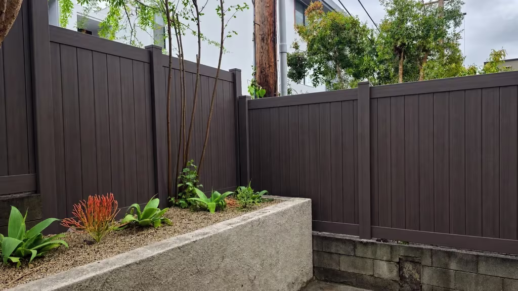 This Dark Walnut vinyl privacy fence forms two runs around a raised stucco planter and a utility pole