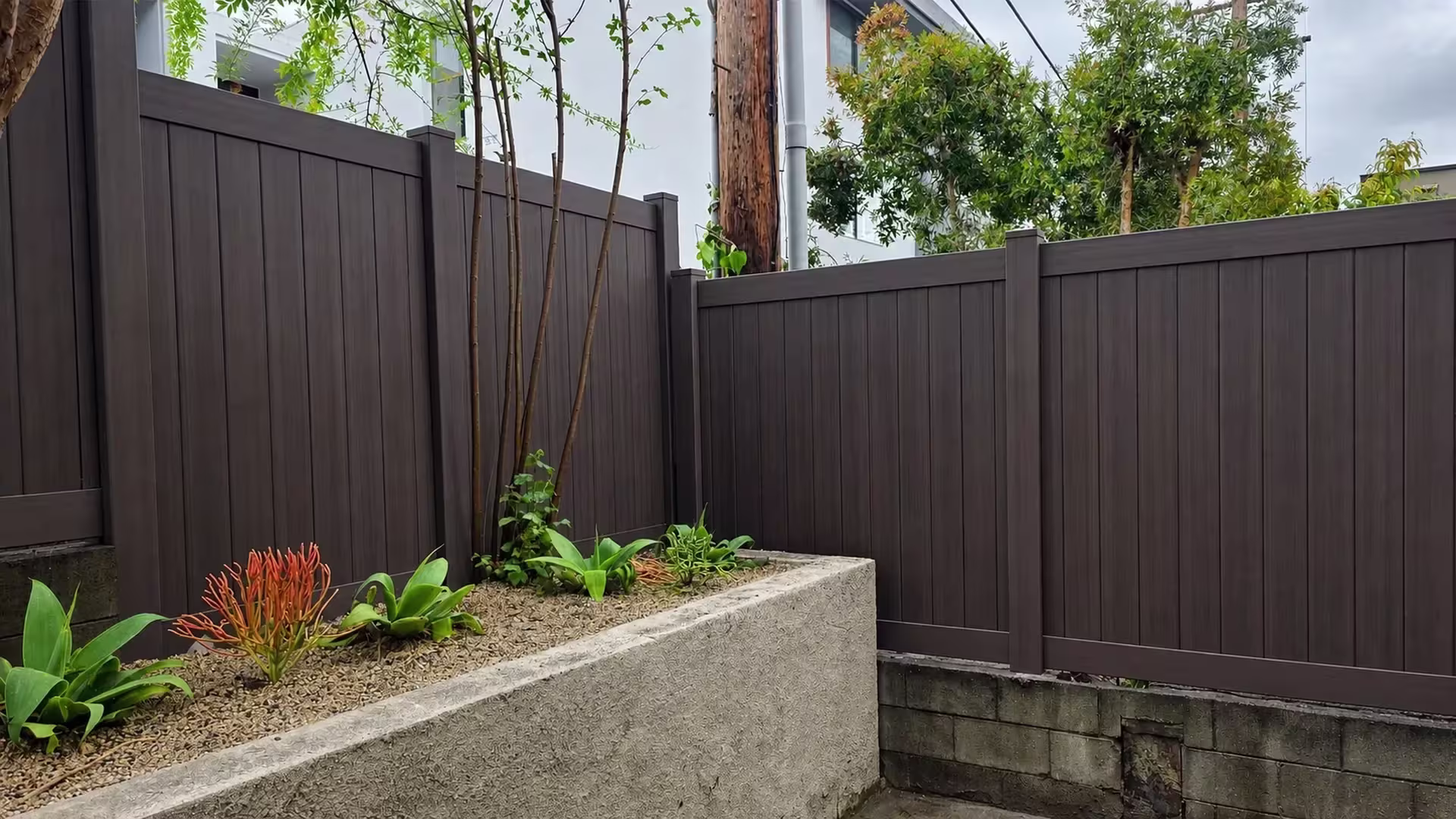 This Dark Walnut vinyl privacy fence forms two runs around a raised stucco planter and a utility pole