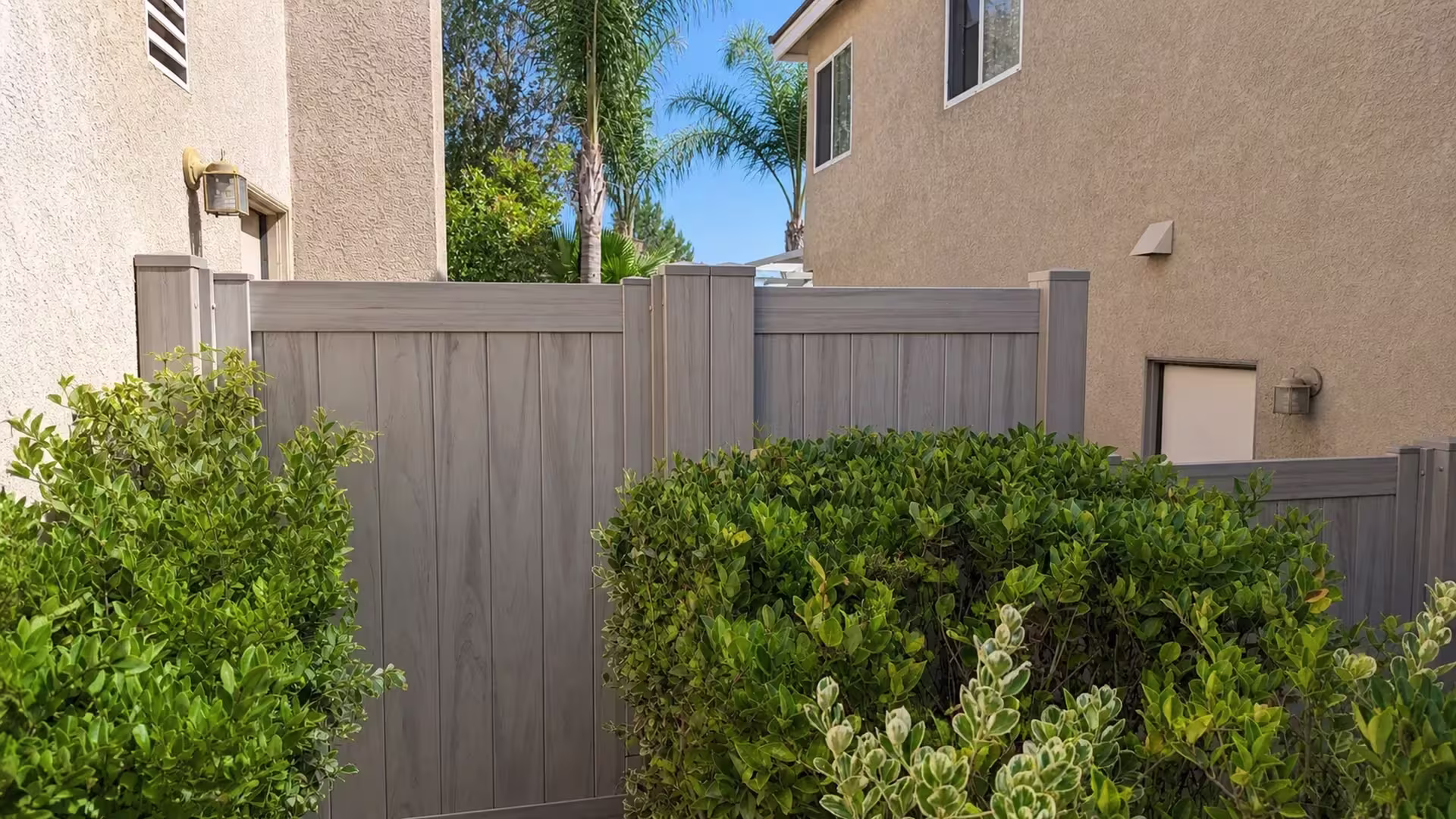 Two tall spans of Mesquite vinyl privacy fence meet at paired center posts beside a trimmed hedge