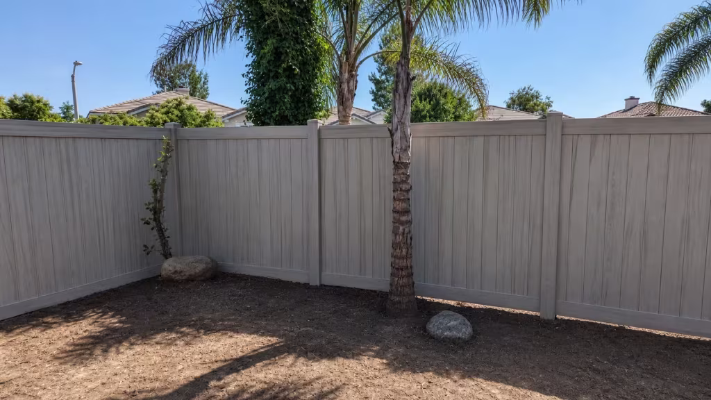 This Mesquite vinyl privacy fence turns a right angle corner behind two palm trunks and landscape rocks