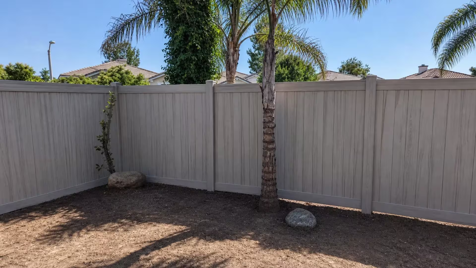 This Mesquite vinyl privacy fence turns a right angle corner behind two palm trunks and landscape rocks