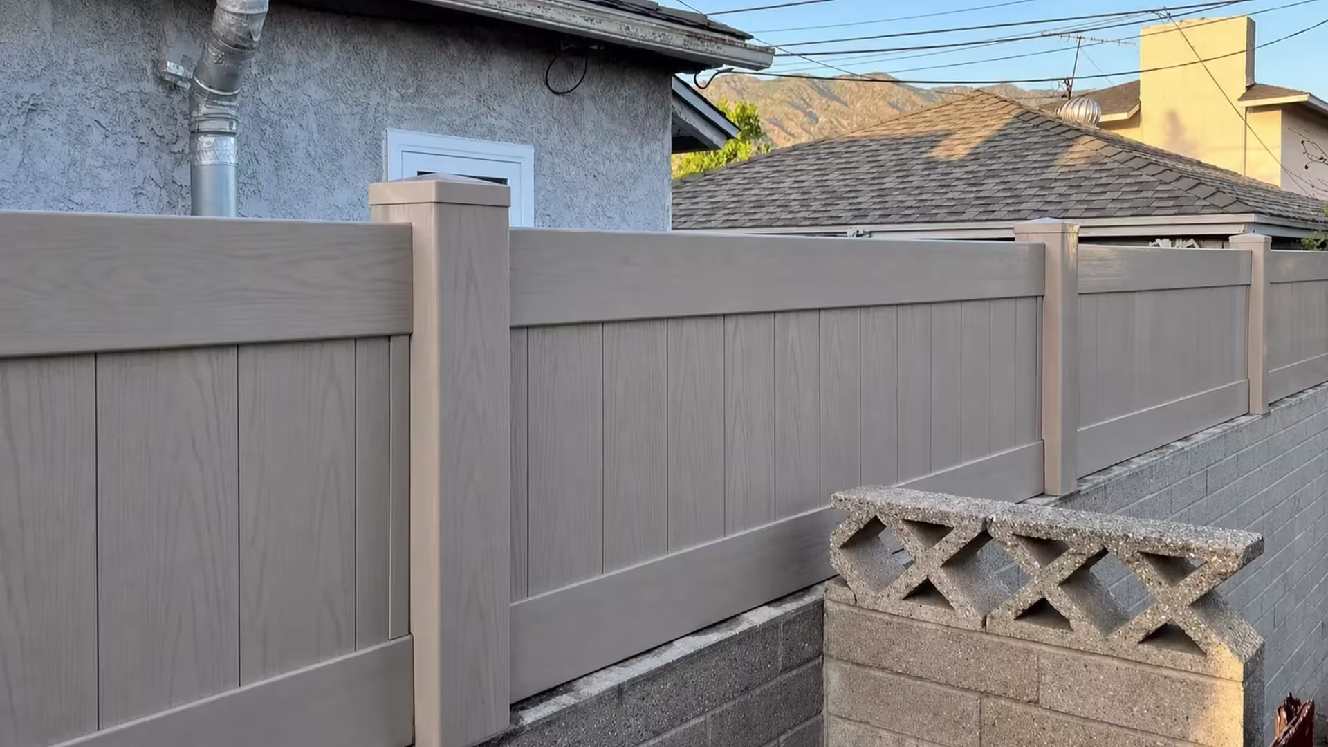Mesquite vinyl vertical privacy fence topping a gray block wall above decorative openwork concrete blocks