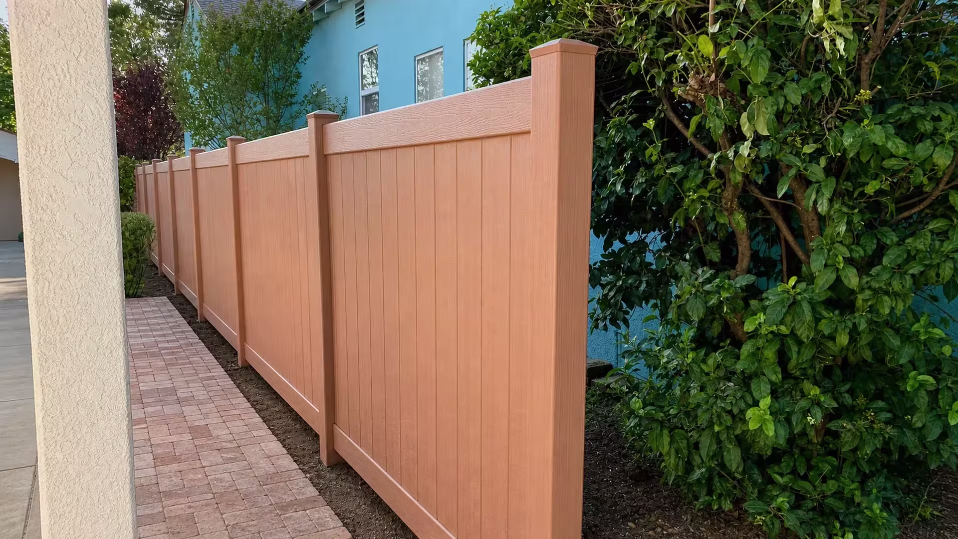 Sierra Blend vinyl vertical privacy fence tracing a brick paver path beside a blue stucco house