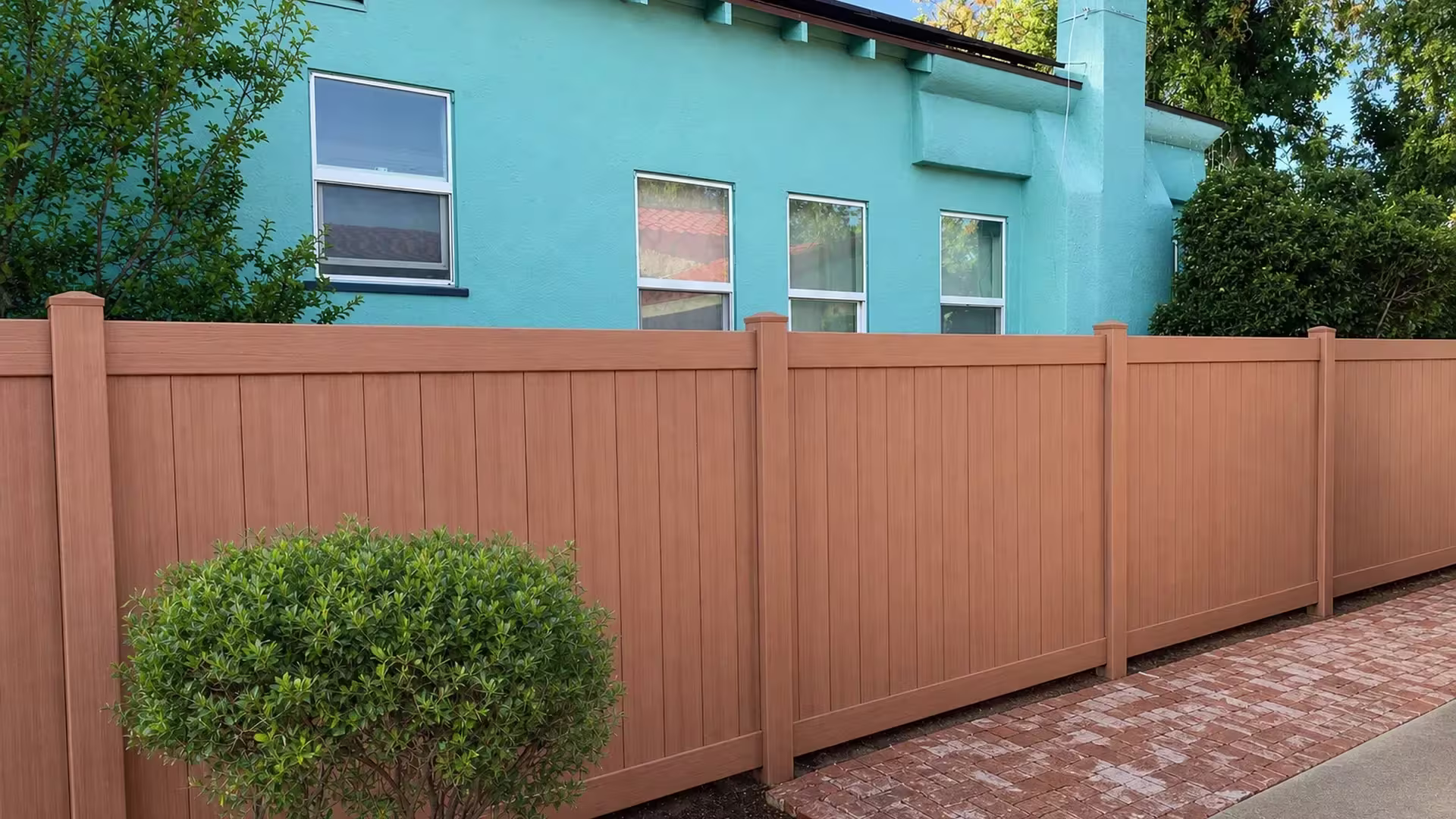 Sierra Blend manufactured-vinyl privacy fence enclosing a yard beneath the chimney of a turquoise stucco house