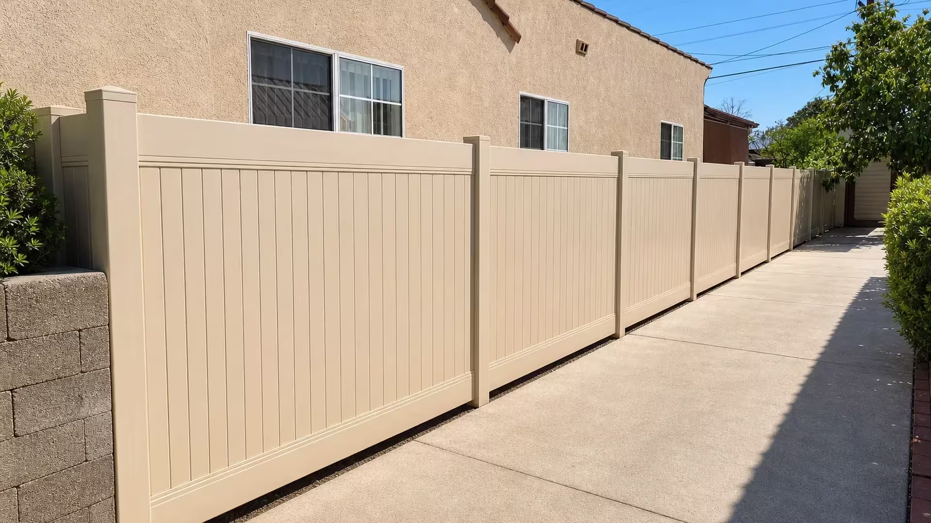 Nine post Tan vinyl vertical privacy fence flanks a concrete driveway beside a block wall