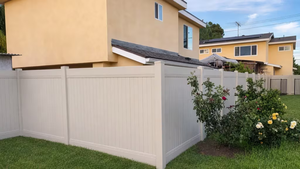 A rose lined L-shaped yard is wrapped by a Tan vinyl vertical privacy fence and planting beds