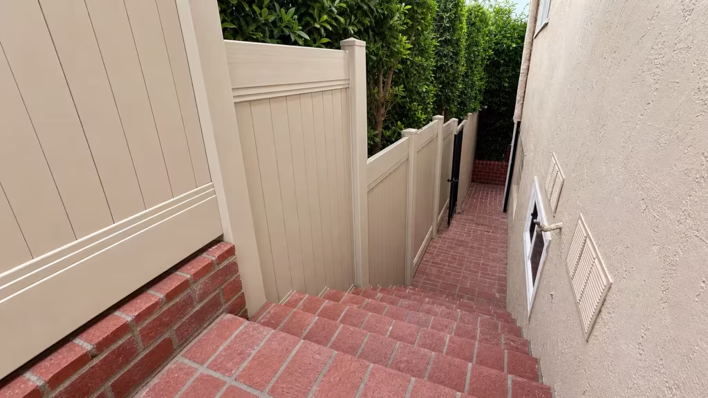 A brick retaining wall and descending brick steps run beside a Tan vinyl vertical privacy fence