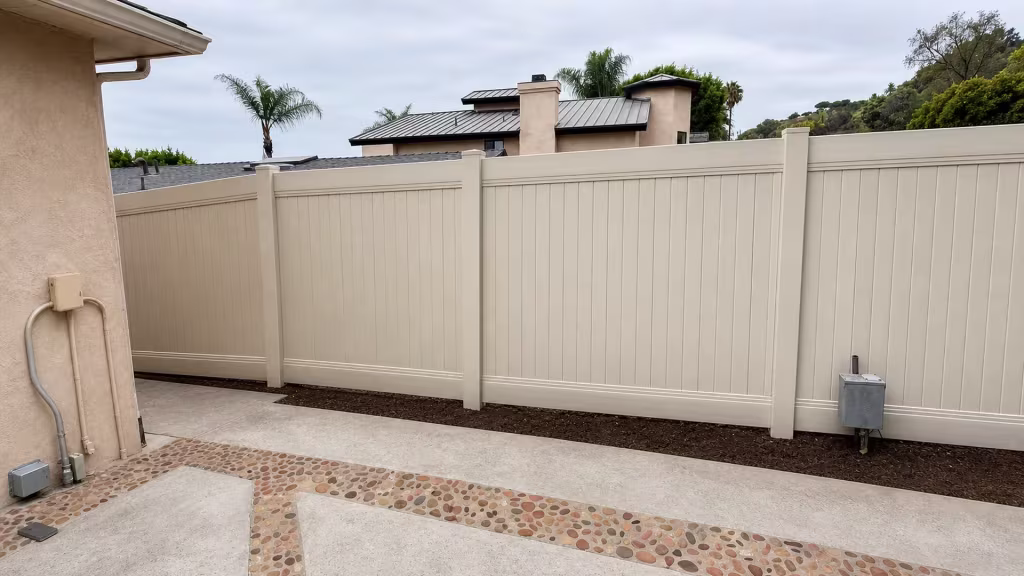 Pebble banded patio paving borders a Tan vinyl vertical privacy fence below a distant hillside