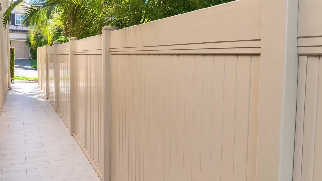 A paver walkway runs beside a Tan vinyl vertical privacy fence with a layered top rail