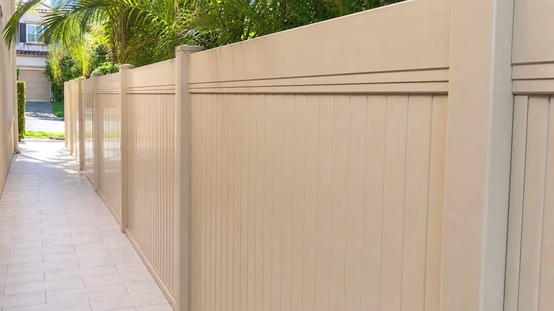 A paver walkway runs beside a Tan vinyl vertical privacy fence with a layered top rail