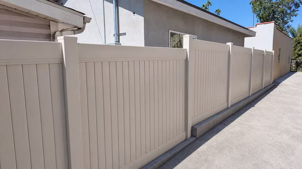 Barred window and concrete curb sit beside a Tan vinyl vertical privacy fence with matching panel construction