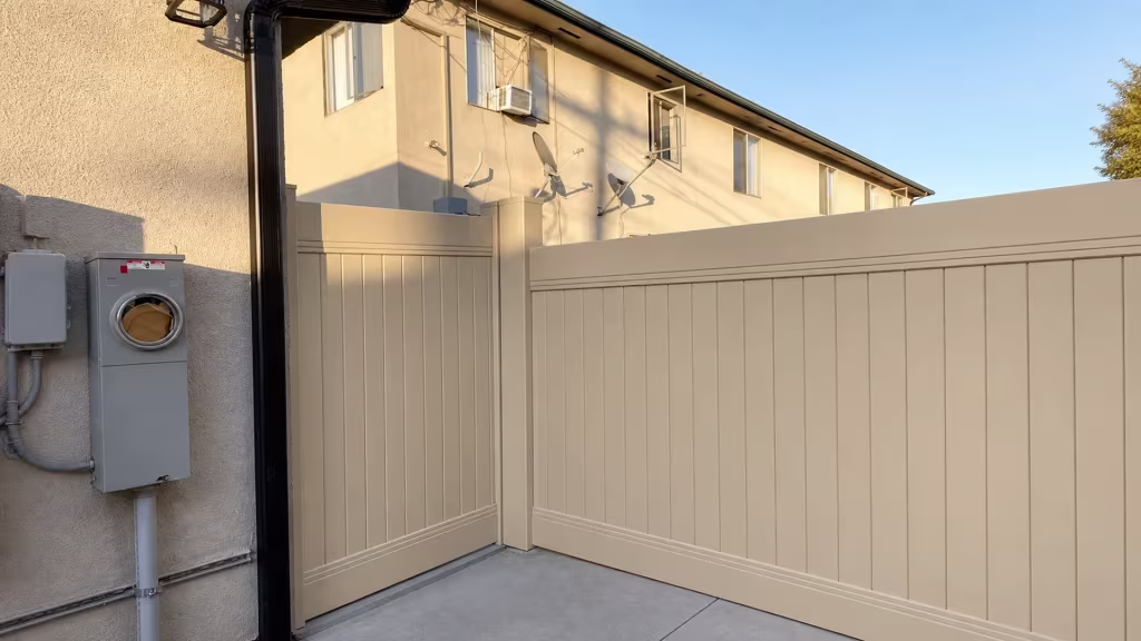 Tan vinyl vertical privacy fence closes off the side yard of a beige stucco multifamily building