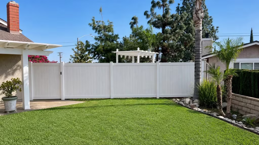 A white arbor rises behind this Weathered Aspen vinyl gate, where the privacy fence continues along the masonry wall