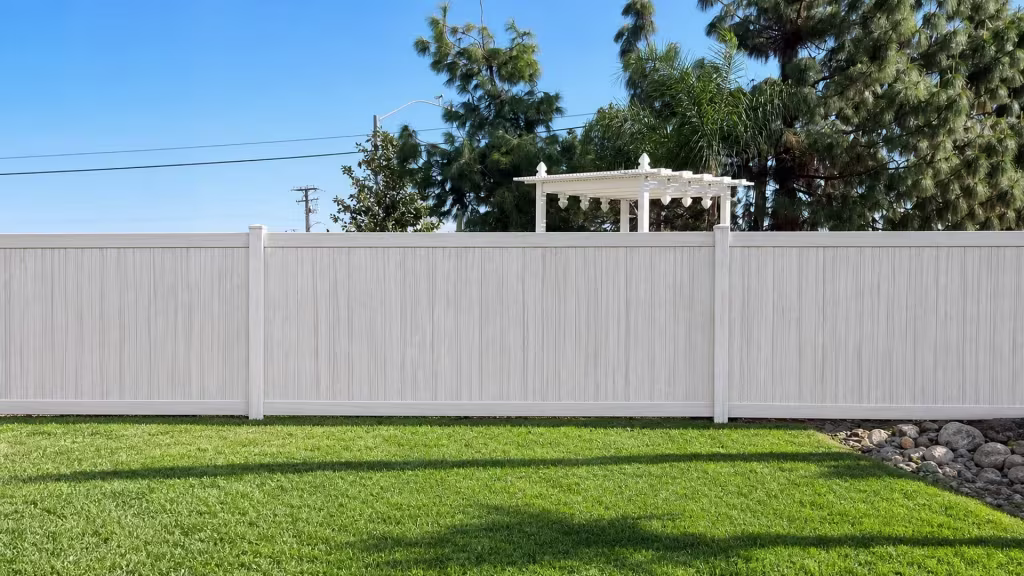 A rock drainage bed borders this Weathered Aspen vinyl privacy fence beneath mature palms and pine trees