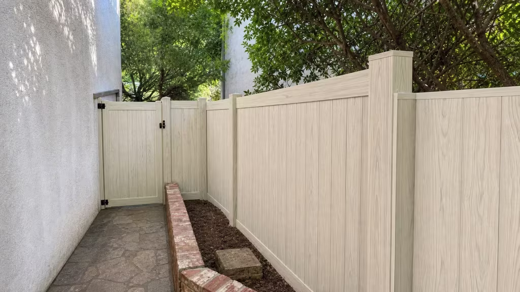 Black hinges anchor this Weathered Aspen vinyl privacy gate to the stucco wall before the fence line turns the corner