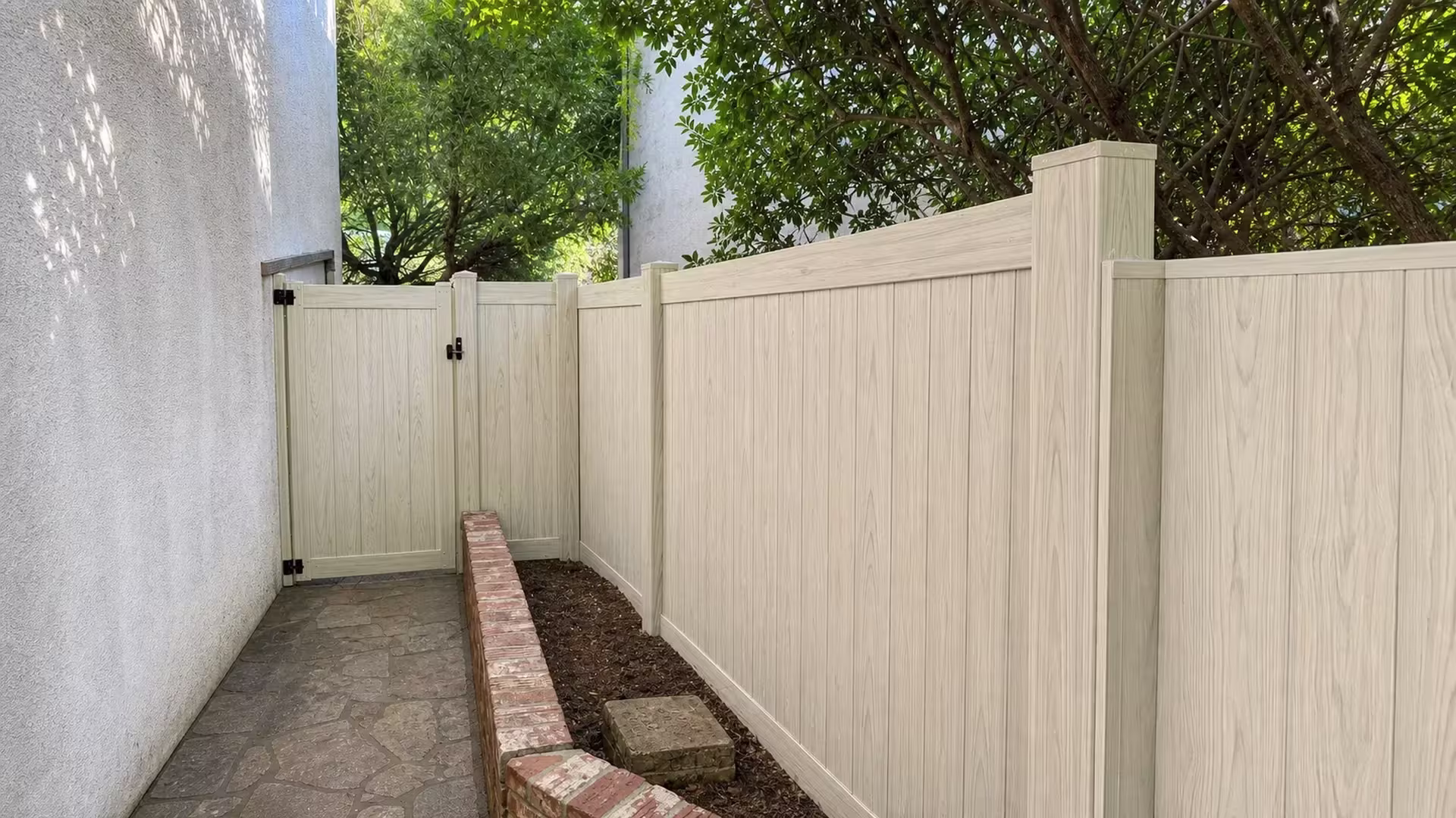 Black hinges anchor this Weathered Aspen vinyl privacy gate to the stucco wall before the fence line turns the corner