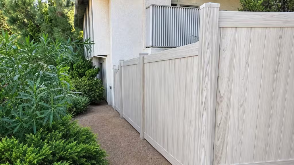 This Weathered Aspen vinyl privacy fence meets a concrete walking surface beside the side yard bin area