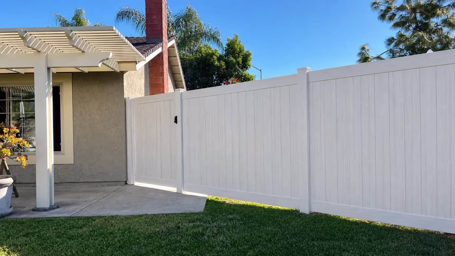 Black latch hardware secures this Weathered Aspen vinyl privacy fence gate beside the house with two panel runs continuing