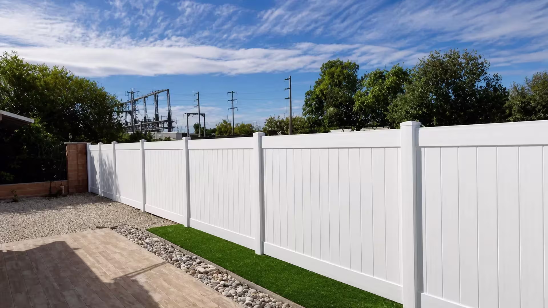White vinyl vertical privacy fence recedes past a pale stone drainage strip and a gravel area