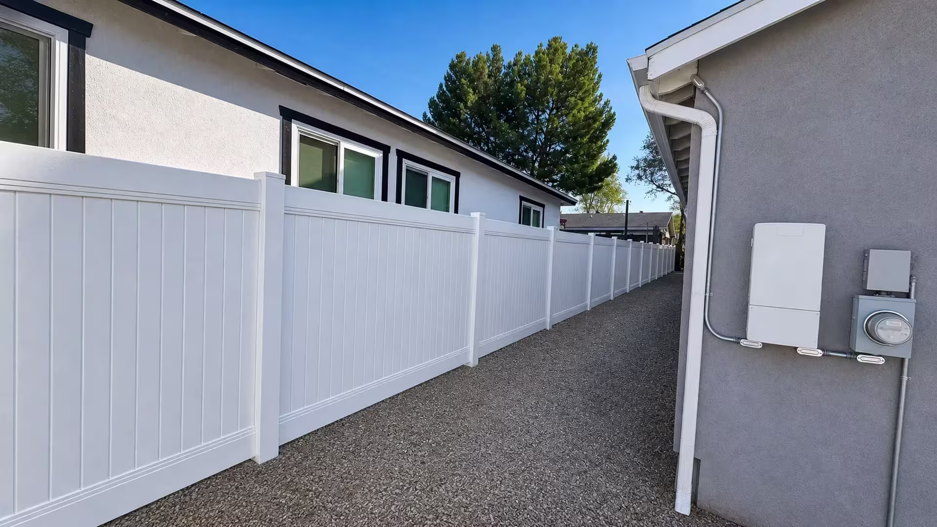 White vinyl vertical privacy fence spans seven posts between two single story buildings
