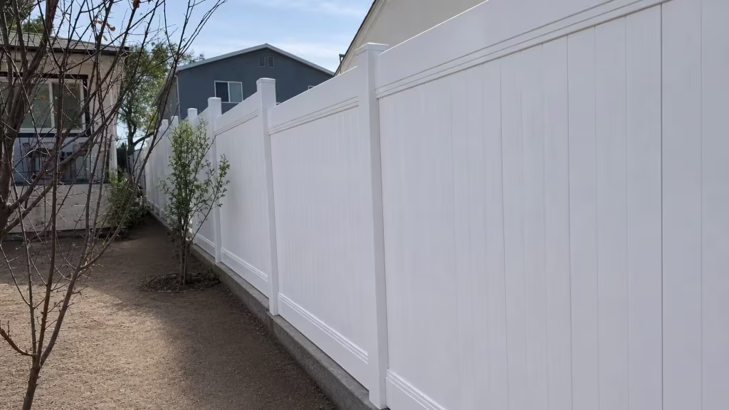 Stepped White vinyl vertical privacy fence rides a dark raised concrete curb beside the adjacent building
