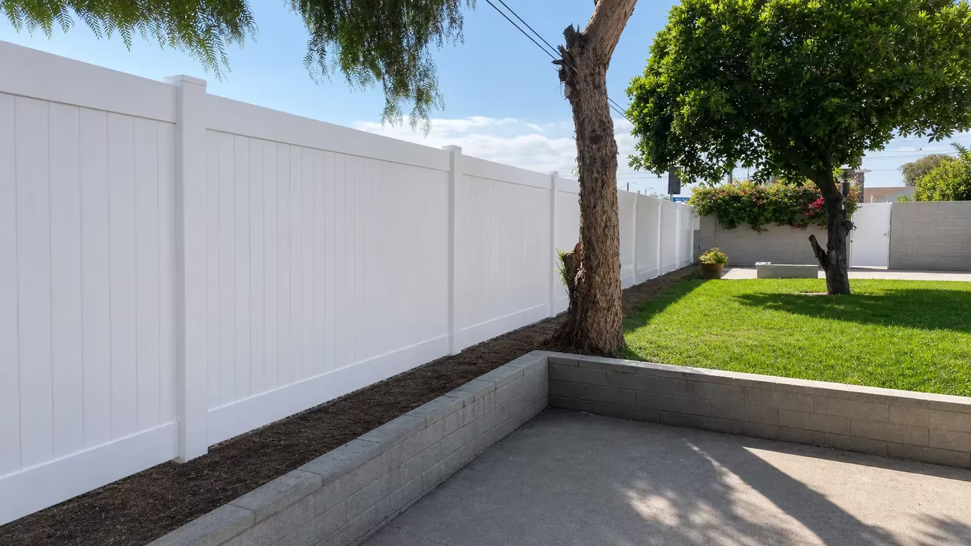 Six posts carry this White vinyl vertical privacy fence past low gray block retaining walls toward the patio