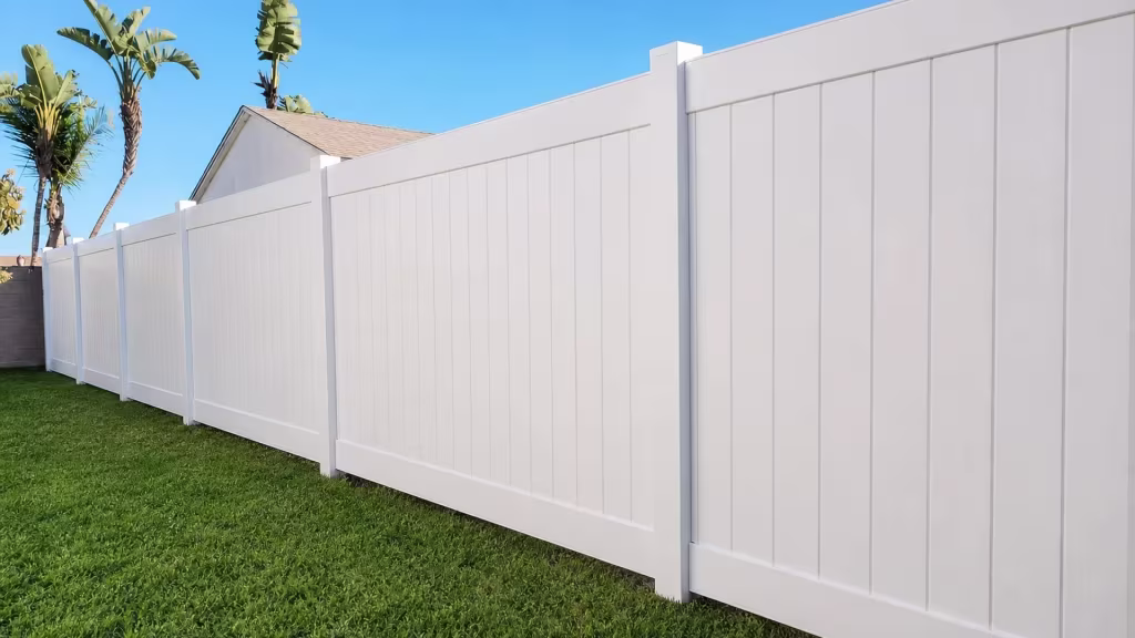White vinyl vertical privacy fence steps down in level stages beside a neighboring gabled building and palms