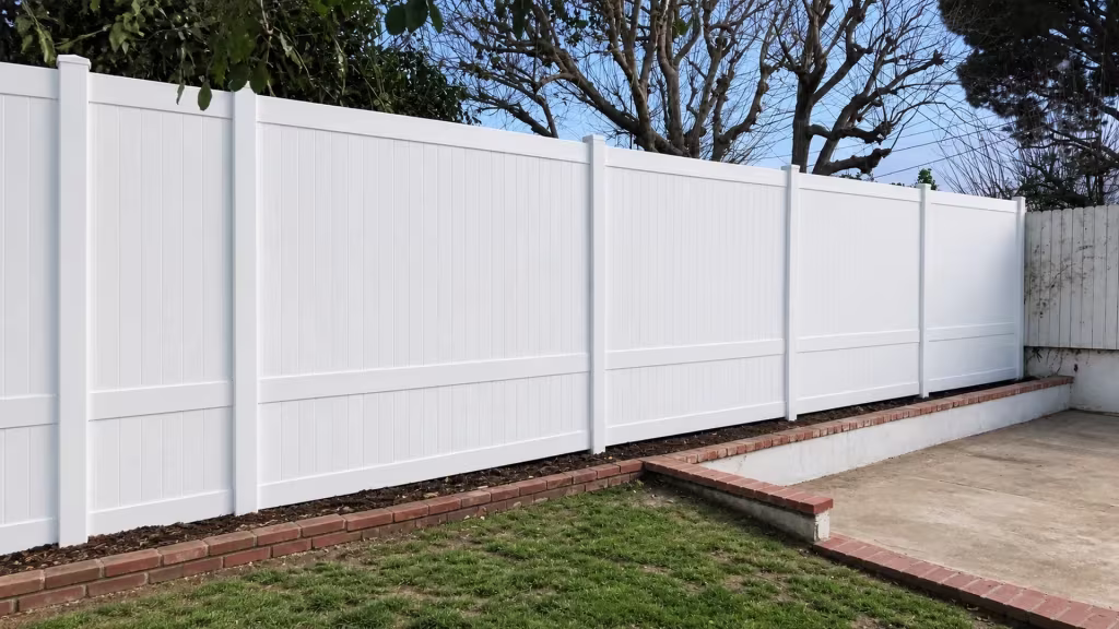 Brick edged walls and an old wood fence flank this White vinyl vertical privacy fence crossing a raised planting strip