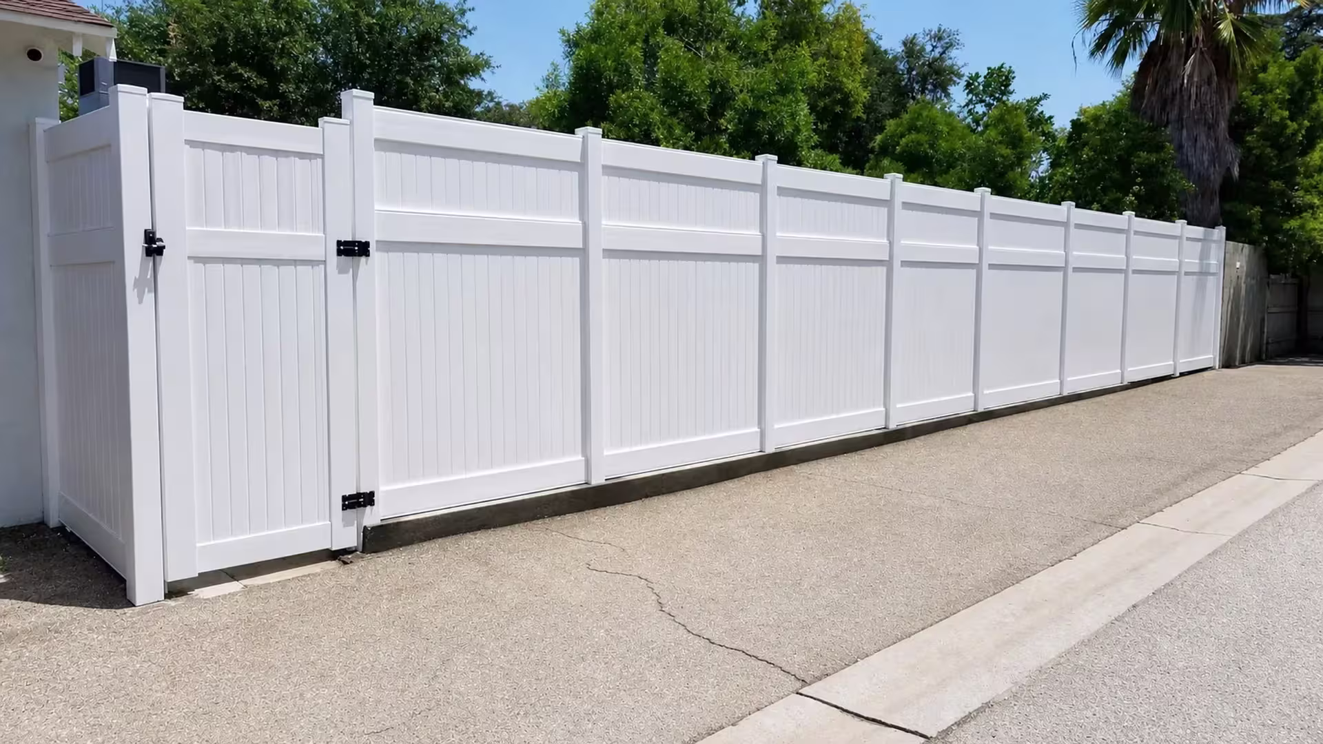 Short White vinyl vertical privacy fence return joins the house near the cracked driveway and curb edge