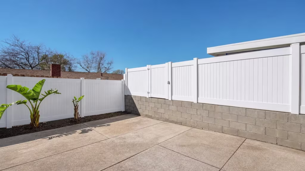 Two banana plants grow beside this White vinyl vertical privacy fence that links to a raised continuing section