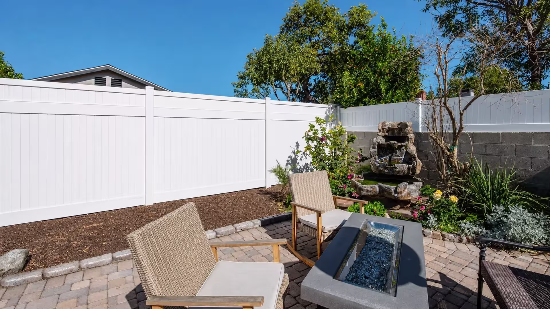 Tiered rock fountain and brick paver patio border this full height White vinyl vertical privacy fence installation