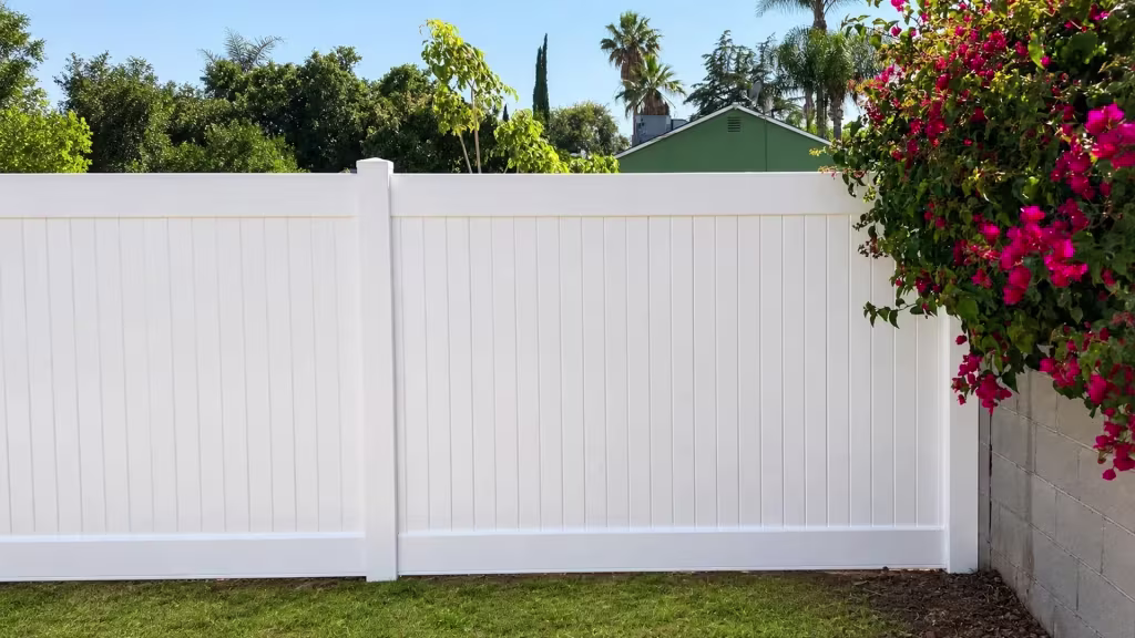 A masonry wall meets this White vinyl vertical privacy fence where bougainvillea partly screens the corner post