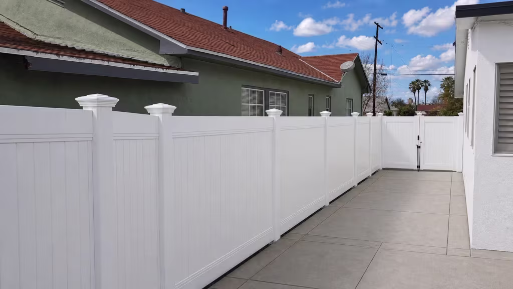 Double leaf White vinyl vertical privacy gate closes a narrow concrete side yard behind seven fence panel bays