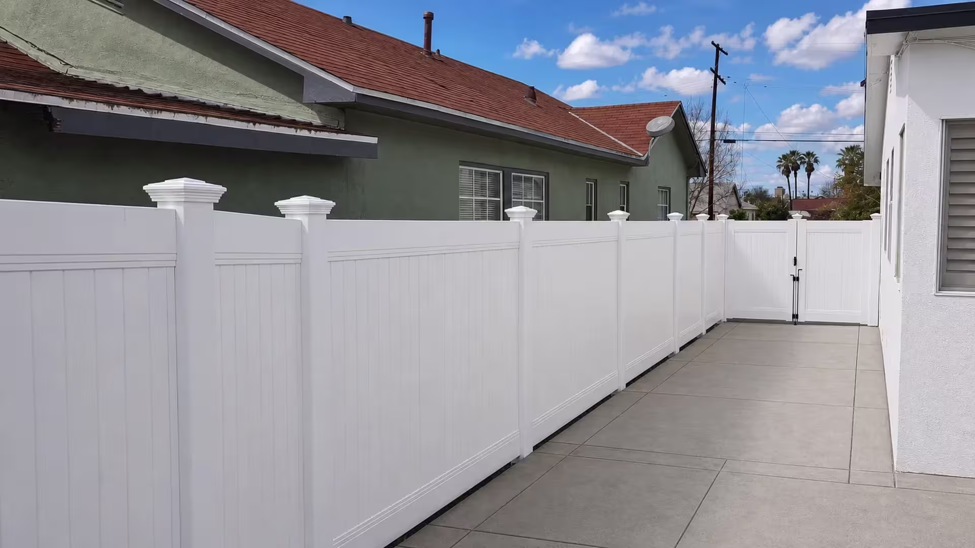 Double leaf White vinyl vertical privacy gate closes a narrow concrete side yard behind seven fence panel bays