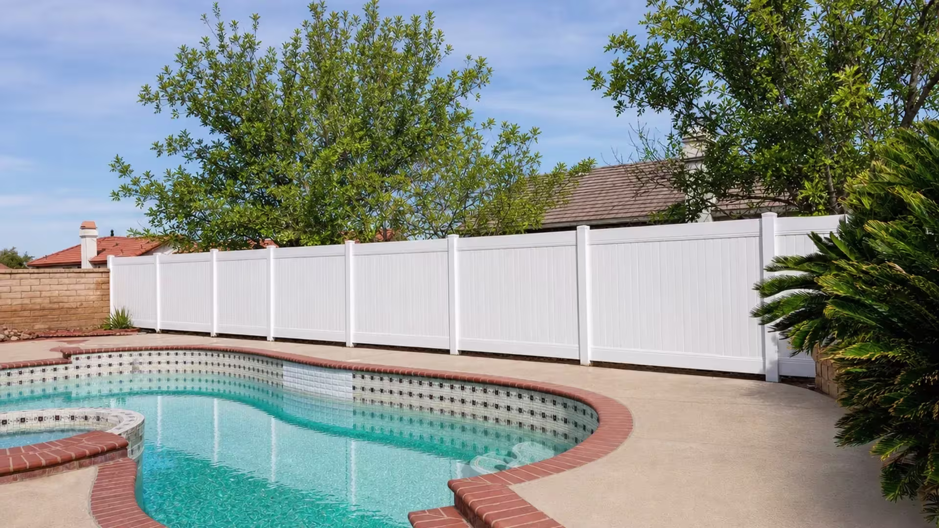 Pool deck bordered by White vinyl vertical privacy fence beside eight posts and established cycads nearby