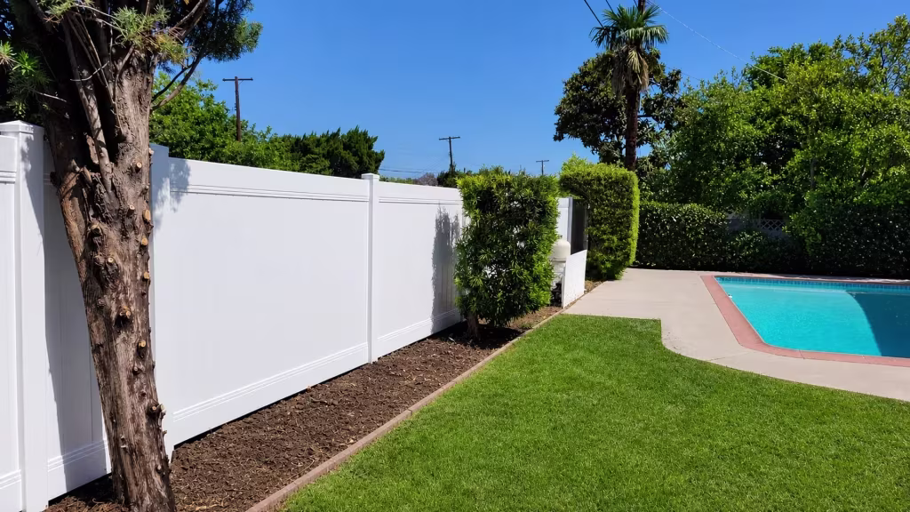 Bright White vinyl vertical privacy fence traces the coping of a brick-edged pool deck