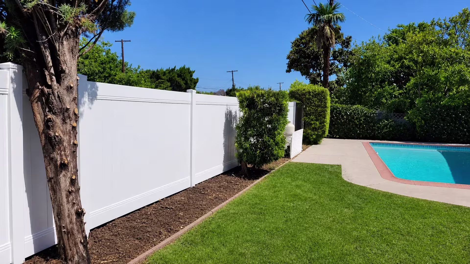 Bright White vinyl vertical privacy fence traces the coping of a brick-edged pool deck
