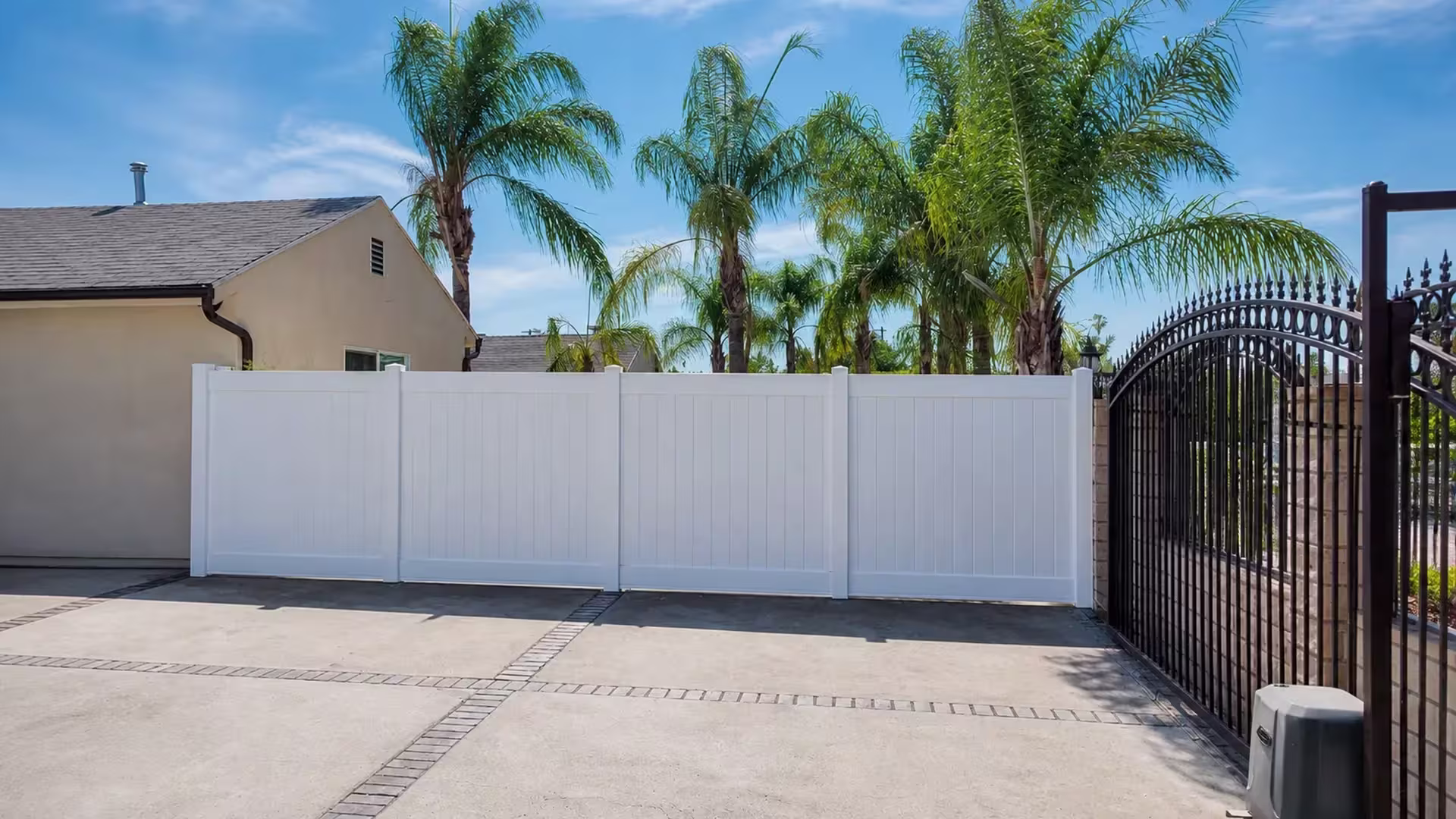Level White vinyl vertical privacy fence tracks a brick-paved driveway past a beige stucco house
