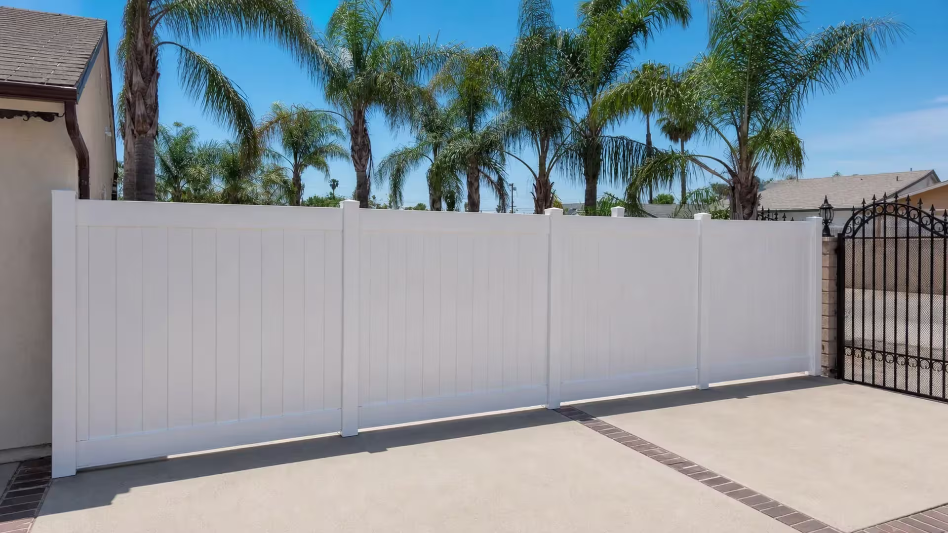 Seamless White vinyl vertical privacy fence crosses a paved driveway in four contiguous panels