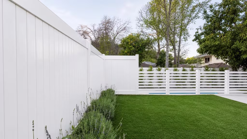 White vinyl privacy fence bordered by lavender planting and a fruiting citrus tree near the pool deck
