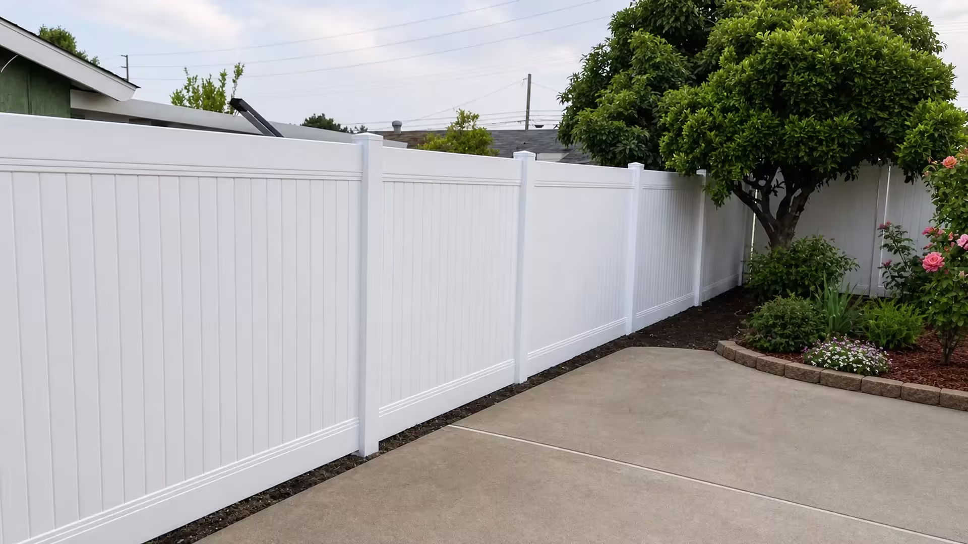 Clean White vinyl vertical privacy fence abuts a concrete patio beneath a mature shade tree