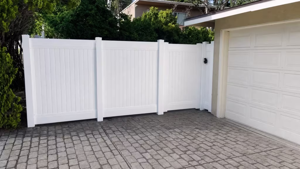 Plain White vinyl vertical privacy fence joins a short return at the garage along a paved driveway