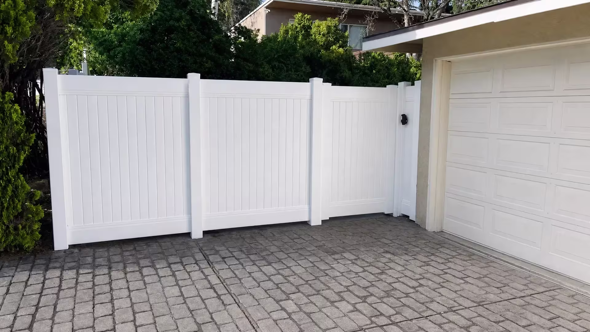 Plain White vinyl vertical privacy fence joins a short return at the garage along a paved driveway