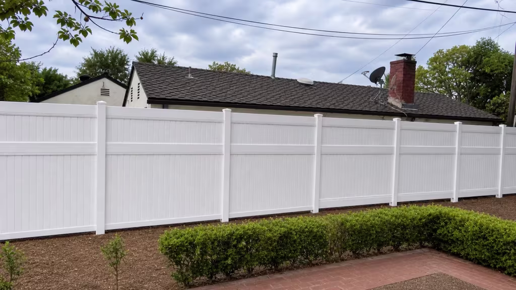 Neat White vinyl vertical privacy fence fronts a brick walkway and trimmed hedge below a gabled roofline