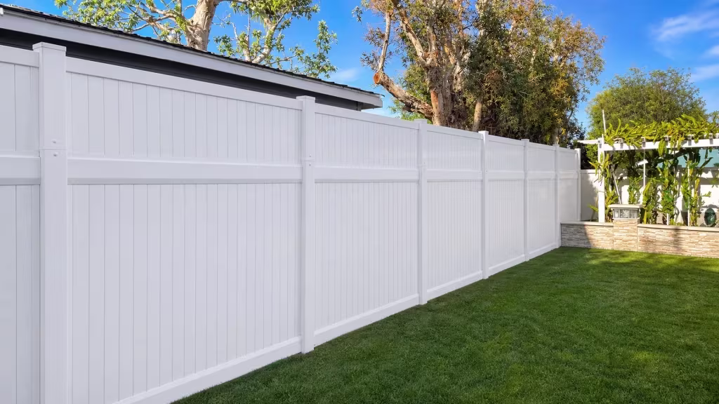 White vinyl privacy fence spans six posts toward a garden structure and raised planter near the eave